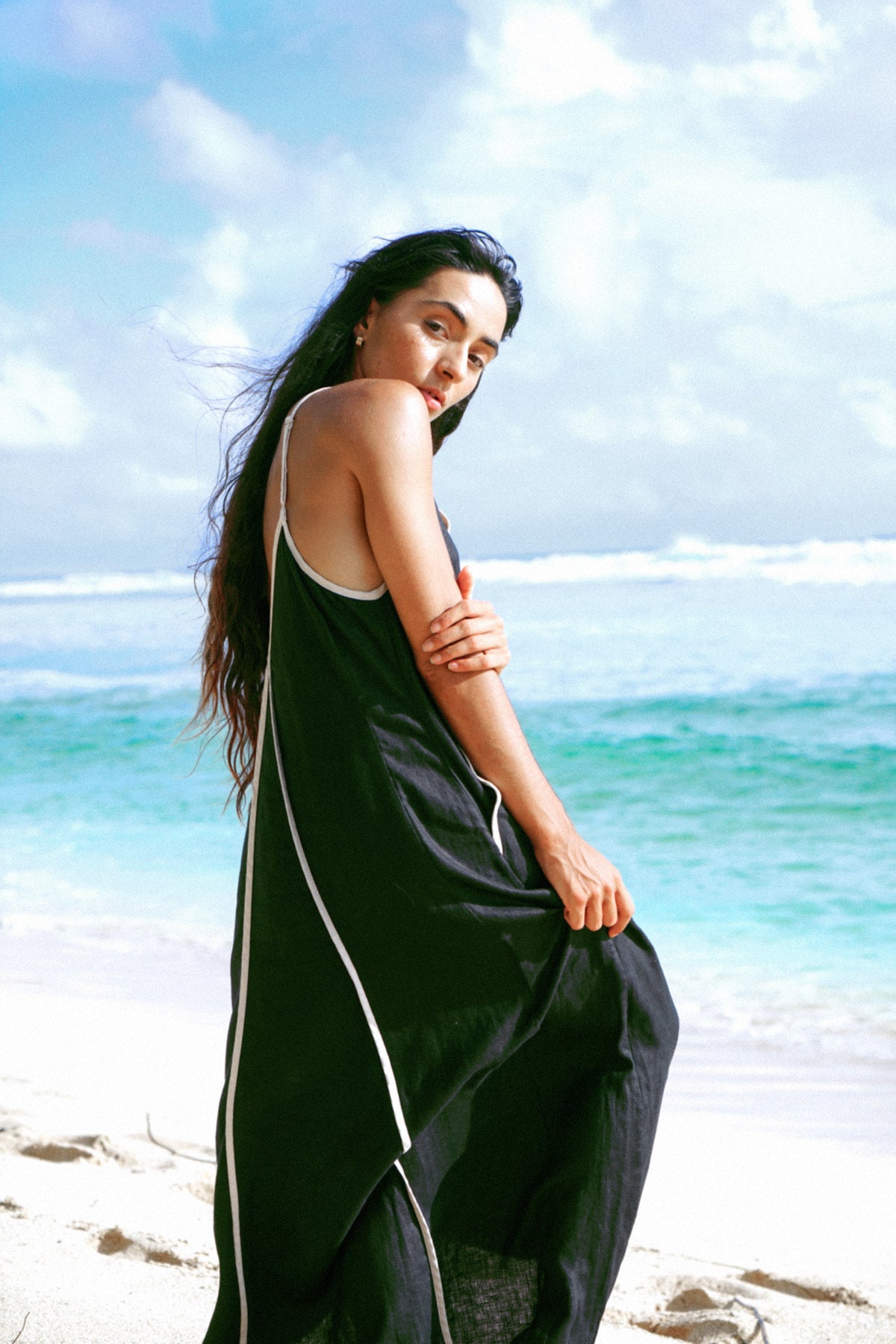 Azalea Linen Maxi Dress in Black - side profile, contrast oatmeal trim and fluid maxi length, beach backdrop - Lilly Pilly Collection