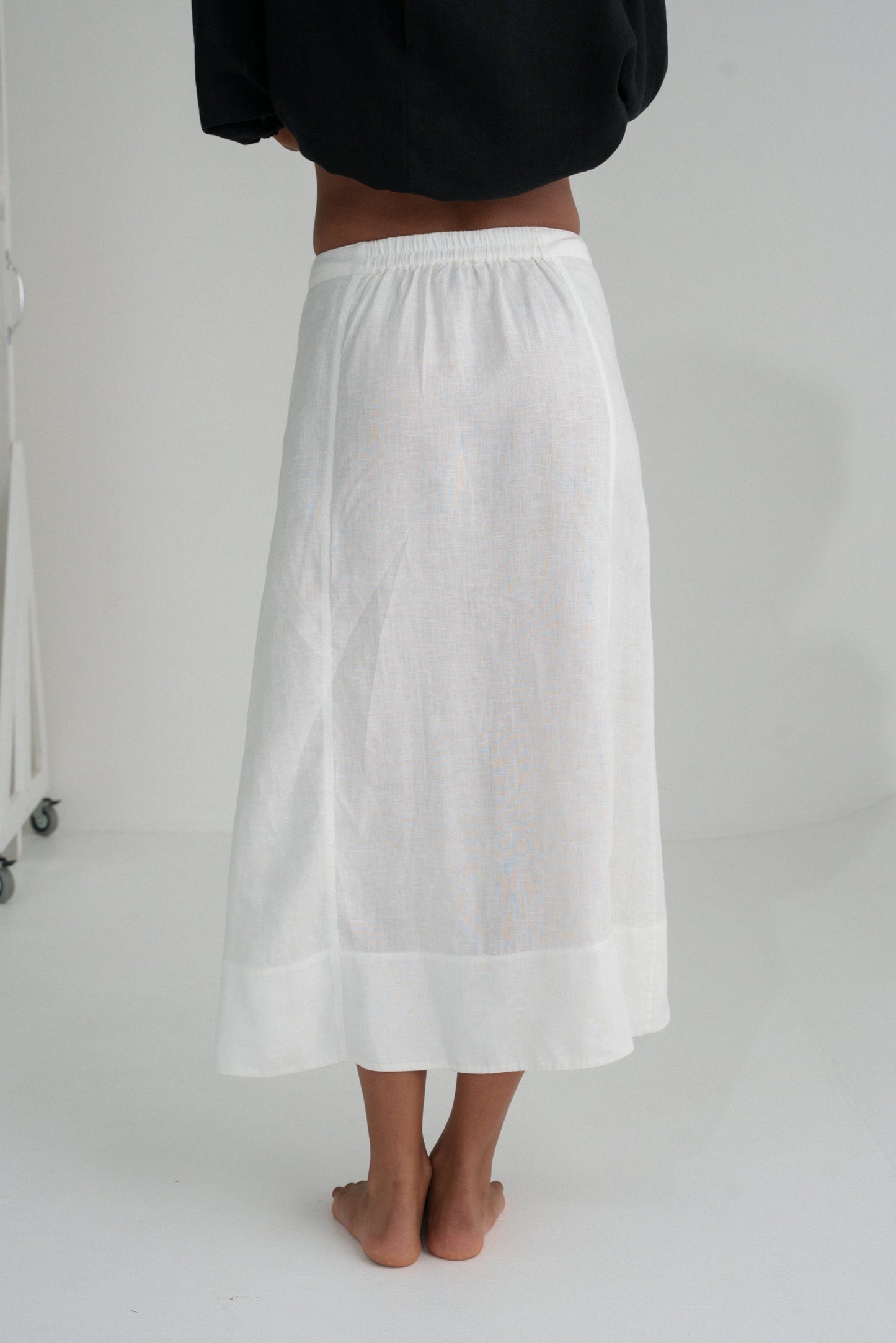 Back view of woman wearing an ivory white Gia linen skirt worn by a person on a plain background