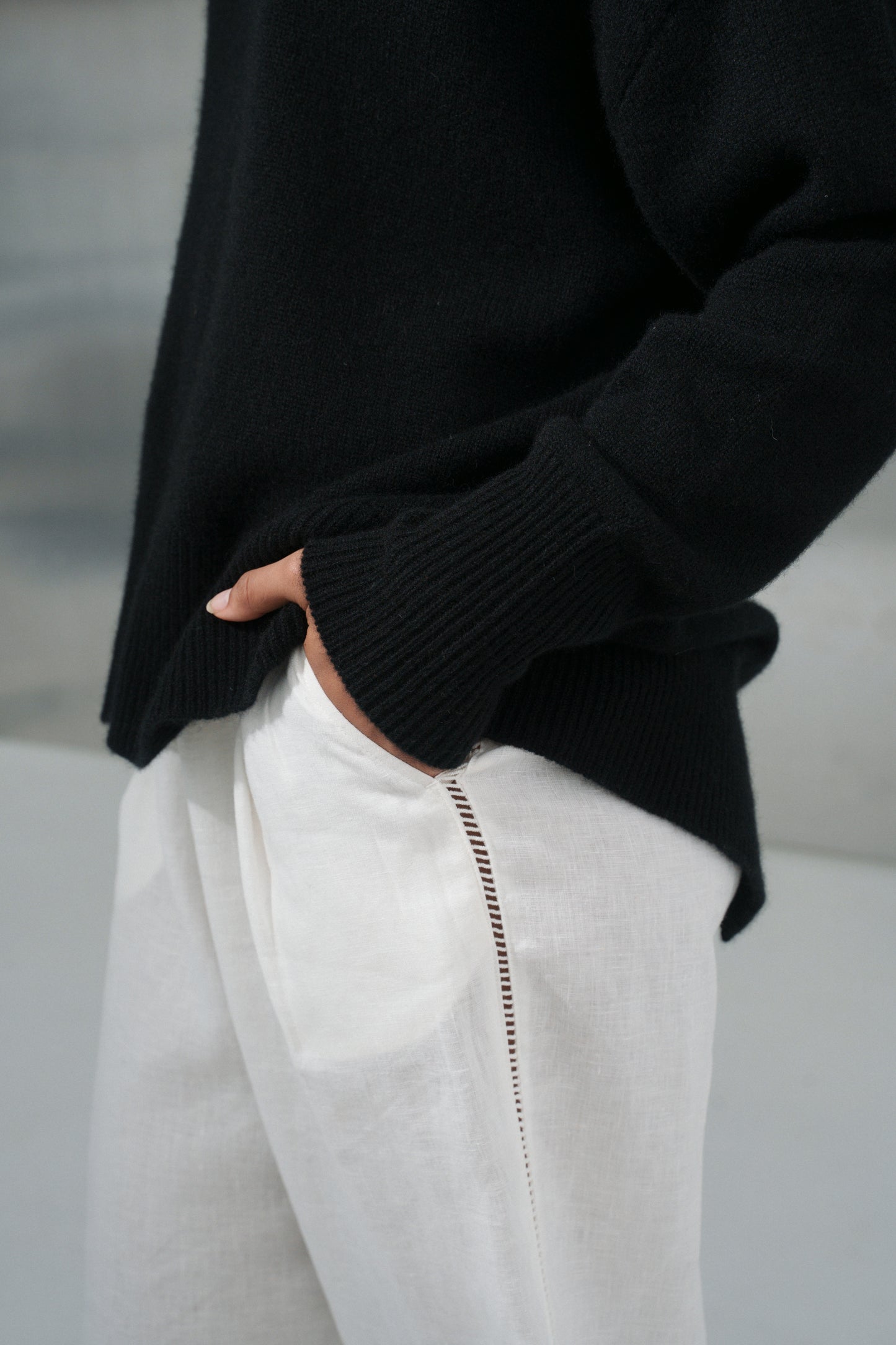 LILLY PILLY woman wearing an black June cashmere knit and ivory linen pants showing sleeve close up view