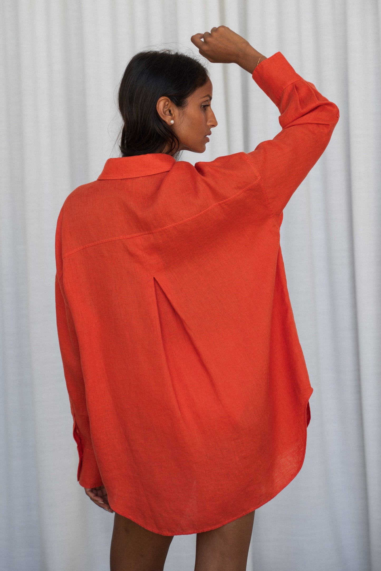 LILLY PILLY woman wearing a spritz Kirra linen shirt leaning against a wooden wall while showing back view