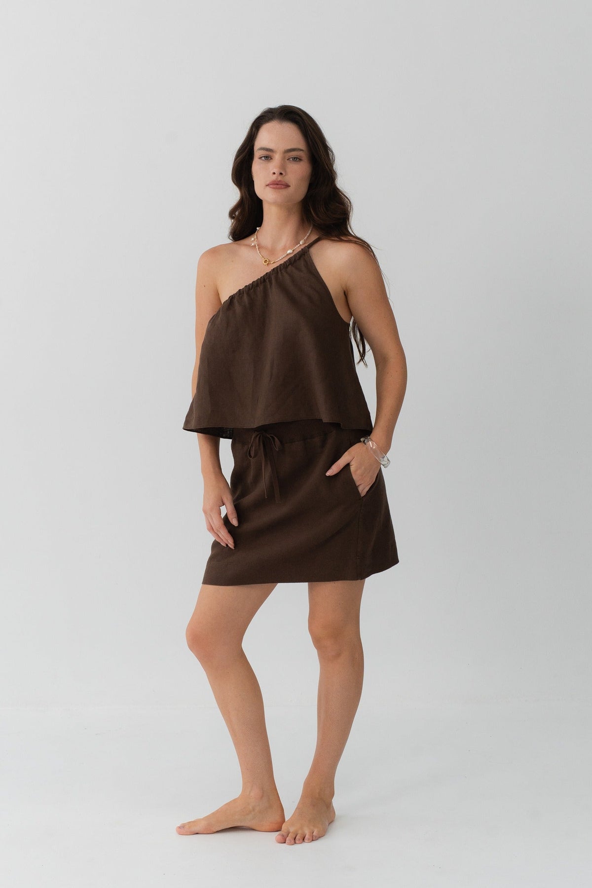 Romy Linen Top in Chocolate - full length front view, one-shoulder neckline, styled with Anelle Linen Mini Skirt in Chocolate, grey studio - Lilly Pilly Collection