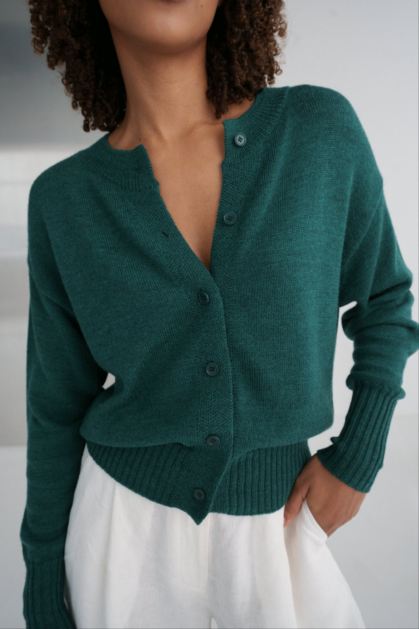LILLY PILLY woman wearing pine green coloured Taylor merino knit cardigan wearing a green cardigan over a white top against a neutral background