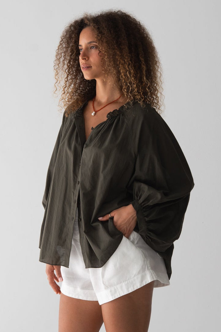 Woman wearing a dark green shirt and white shorts against a plain background side view