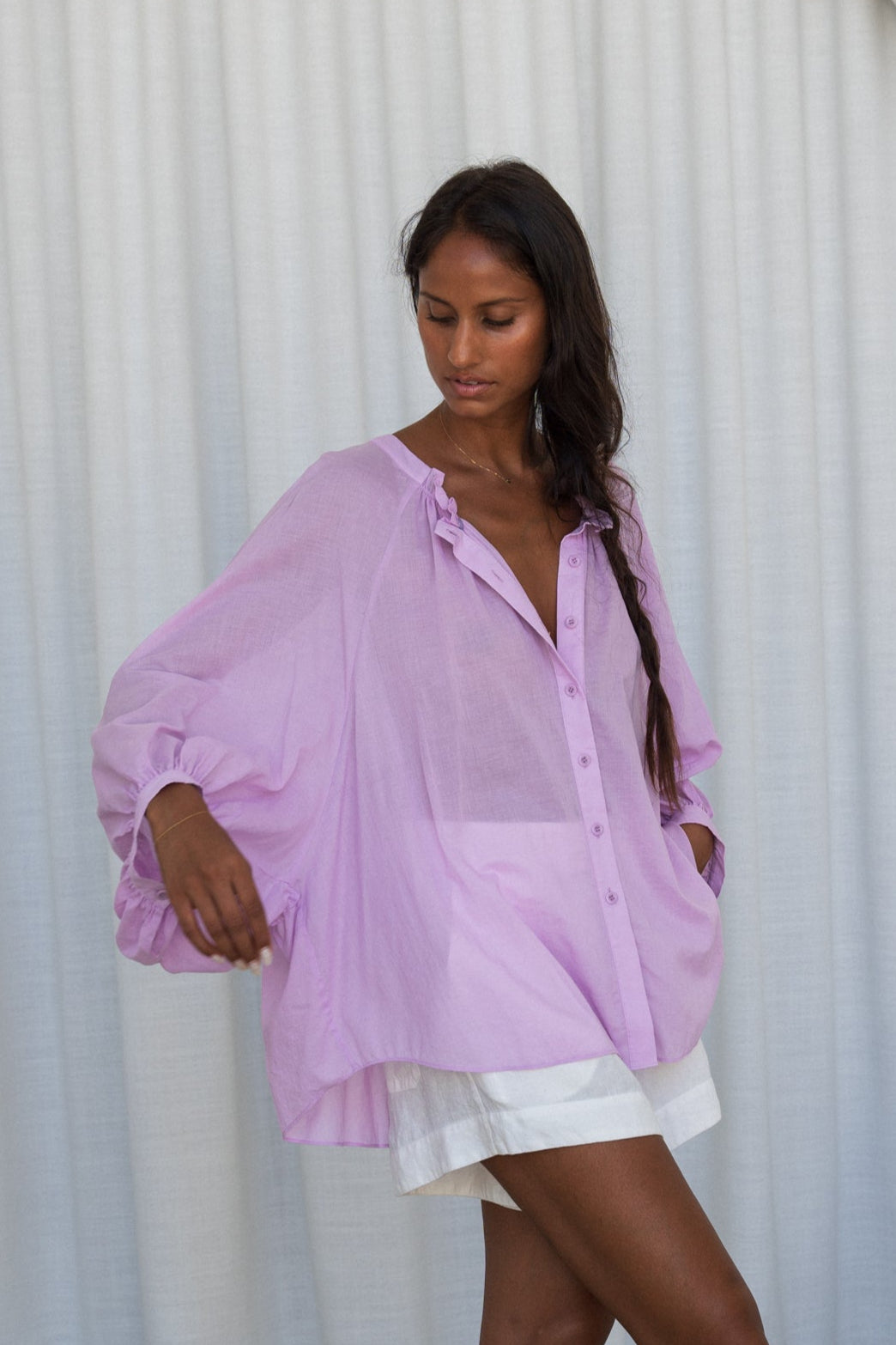 LILLY PILLY woman wearing a orchid Thalia cotton voile shirt blouse showing side view in front of a curtain background