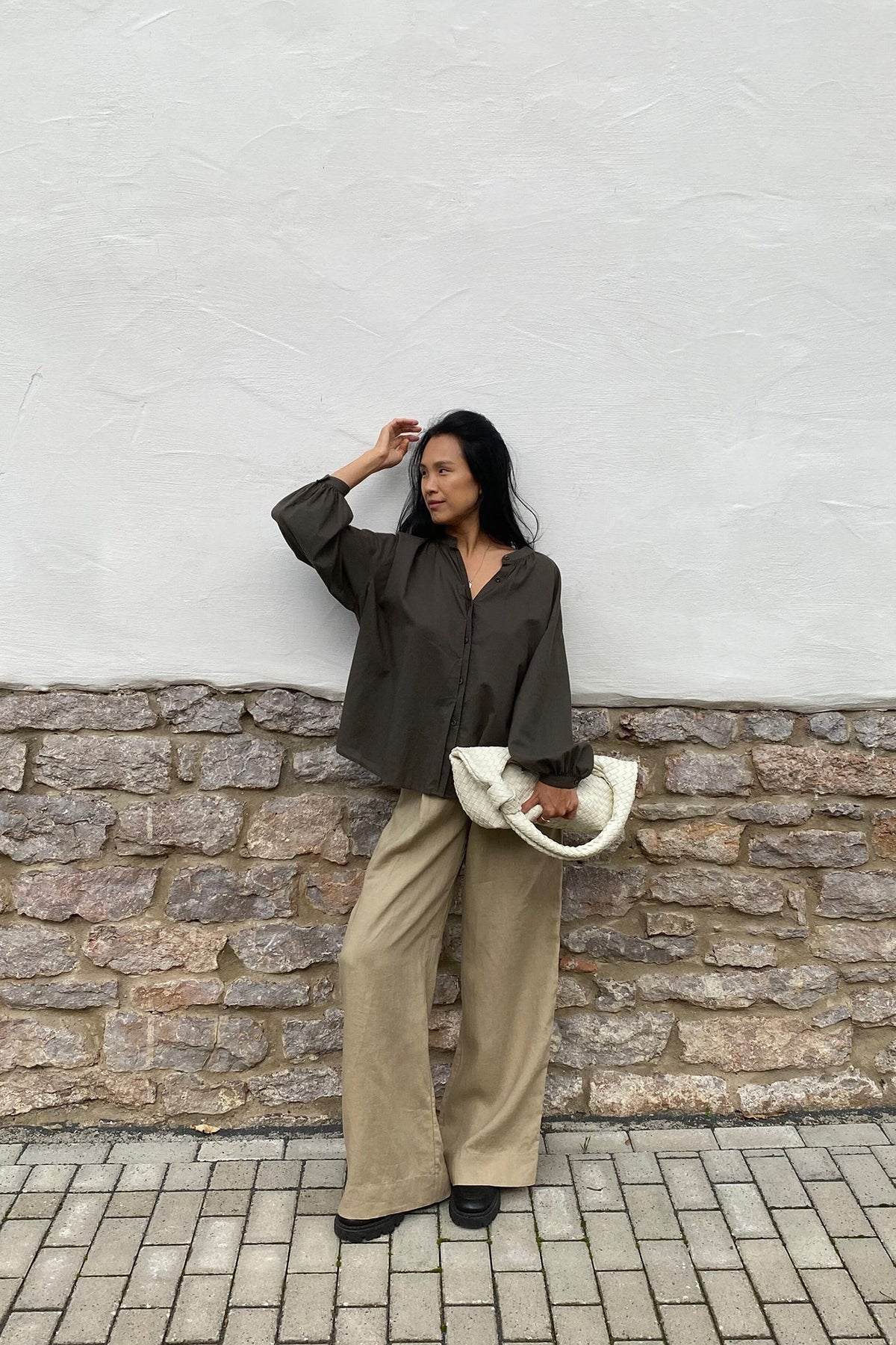 Woman in a green shirt and beige pants standing against a white wall with a stone ledge.