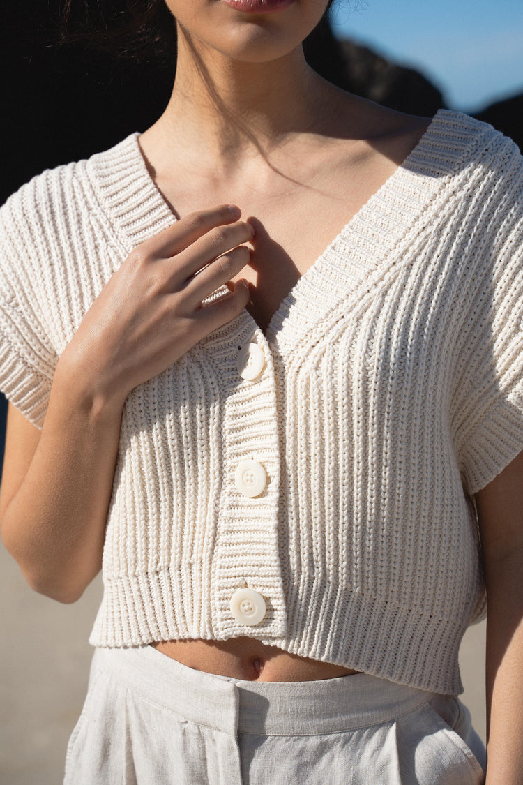 Elara Cotton Vest in Cream - close-up, V-neckline and button-front detail, standing on beach - Lilly Pilly Collection