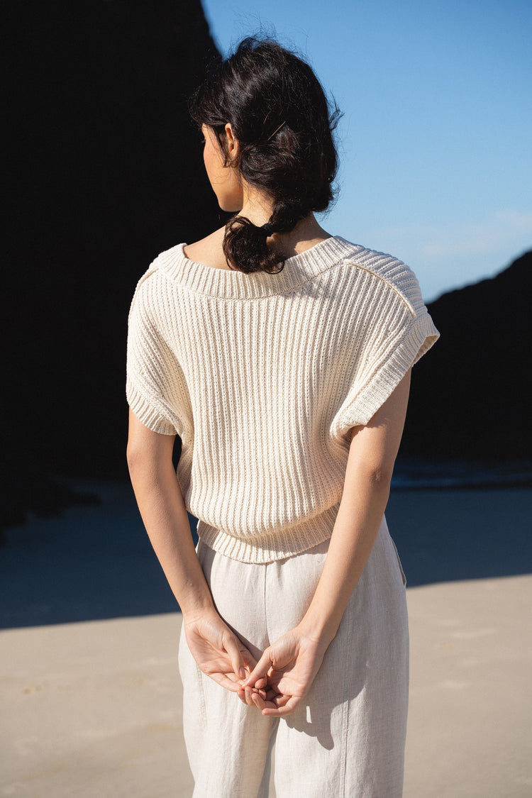 Elara Cotton Vest in Cream - back view, ribbed knit collar detail, standing on beach - Lilly Pilly Collection