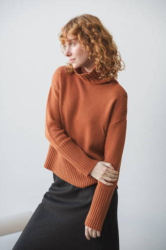 Kaida Cashmere Knit in Cajun Red - three quarter view paired with black Riley skirt standing by a white studio wall - Lilly Pilly Collection