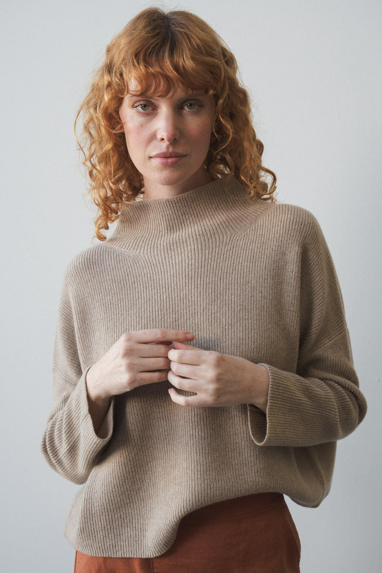 Lumi Cashmere Knit in Oatmeal - front view, funnel neckline, ribbed knit detail, worn with rust skirt, studio setting - Lilly Pilly Collection