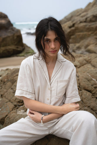 Quinn Linen Shirt in Chalk White - close up front view while seated on the rocks, paired with matching Rika pants - Lilly Pilly Collection