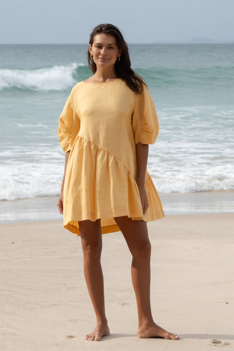 Layla Linen Short Dress in Butter Yellow - full length front view, round neckline and puff sleeves, standing on beach with ocean backdrop - Lilly Pilly Collection