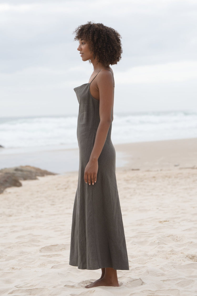 Allegria Bias Linen Maxi Dress in Khaki - side profile, full length, standing on beach with ocean backdrop - Lilly Pilly Collection