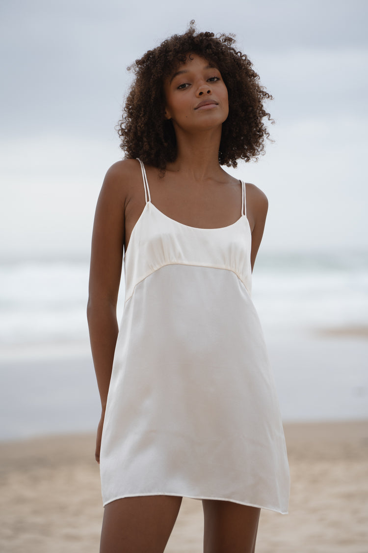 Ella Silk Mini Slip Dress in Ivory - front view close-up, scoop neckline and spaghetti straps, standing on beach - Lilly Pilly Collection