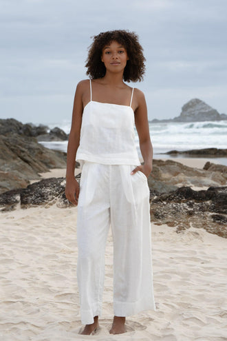 Ivy Linen Crop Pants in Ivory - full length front view, woman wearing Ivory wide-leg linen crop pants with matching ivory linen cami, sandy beach with coastal rocks backdrop - Lilly Pilly Collection