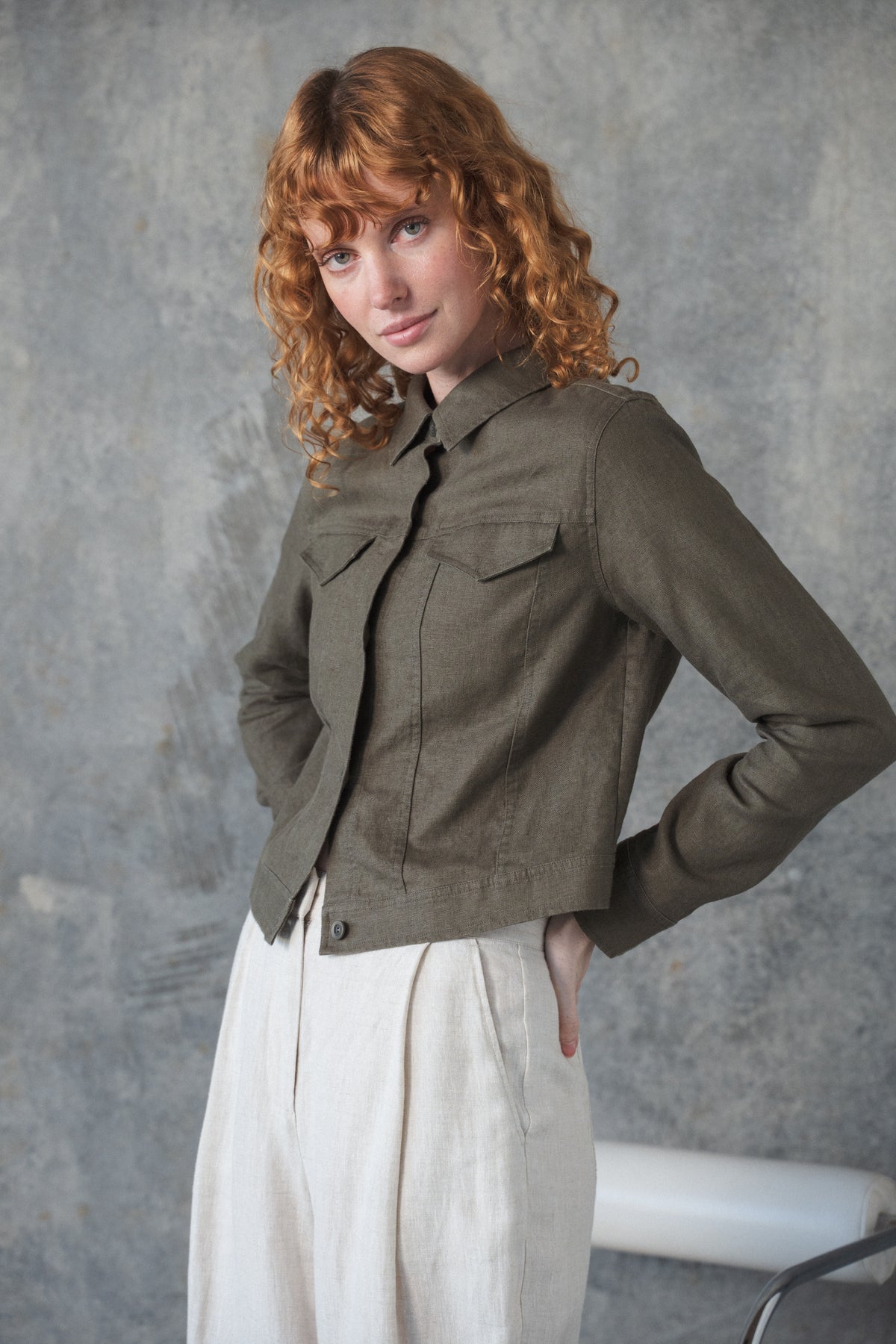A woman modeling a MILLY khaki linen jacket with denim-inspired details, eco-friendly Corozo nut buttons, and front pockets.