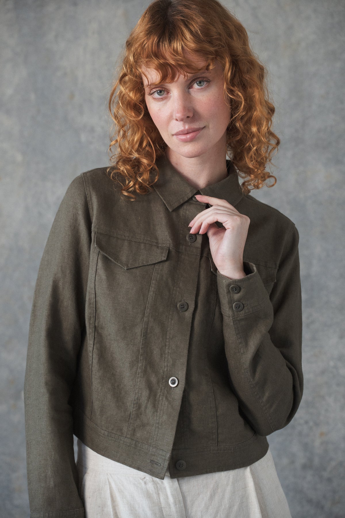Close up of woman modeling a MILLY khaki linen jacket with denim-inspired details, Corozo nut buttons, and front pockets.