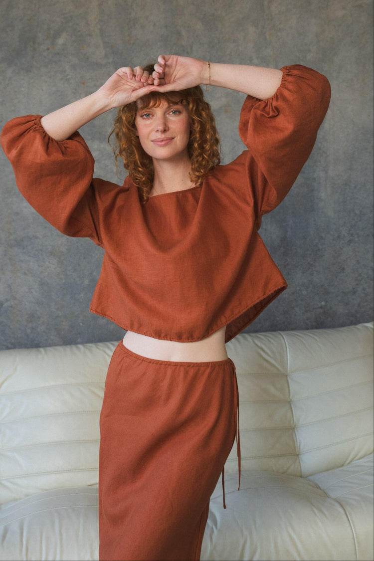 Louisa Linen Top in Cajun Red - front view, hands above head, boat neckline and balloon sleeves, worn with matching tie-waist skirt, studio setting - Lilly Pilly Collection