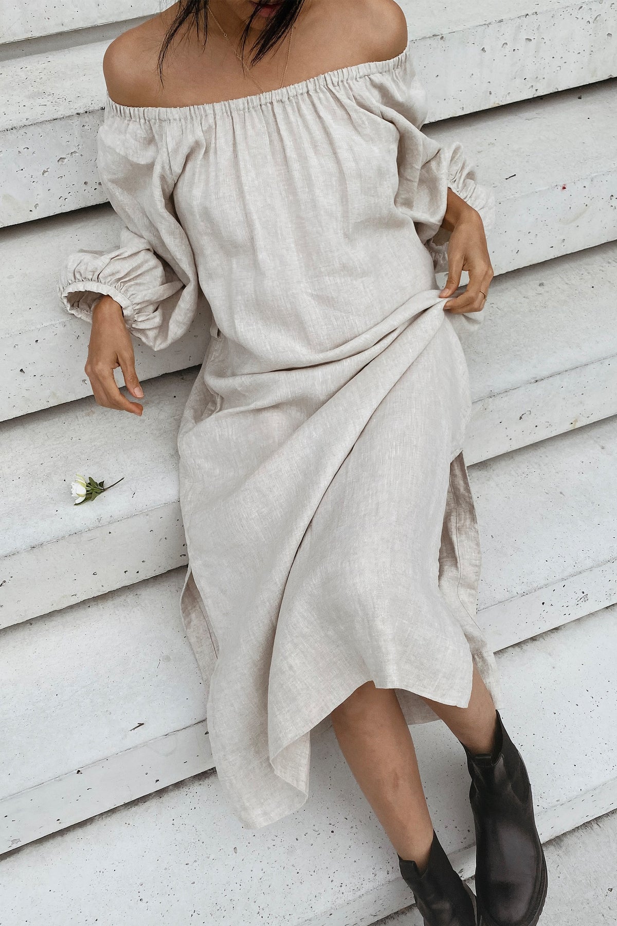 Lucia Linen Midi Dress in Oatmeal - close-up detail, off-shoulder elasticated neckline and gathered sleeve, model seated on concrete steps - Lilly Pilly Collection