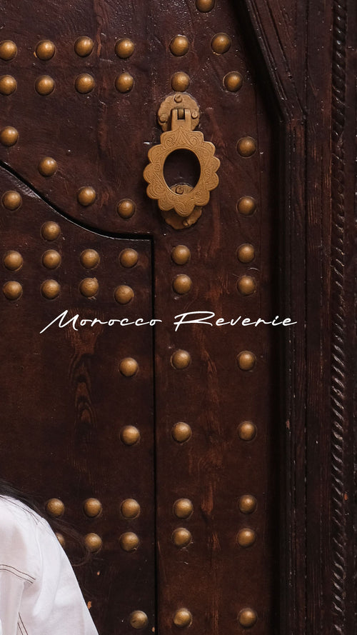 Close-up of a wooden door with brass studs and a handle, featuring the brand 'Morocco Reverie'.