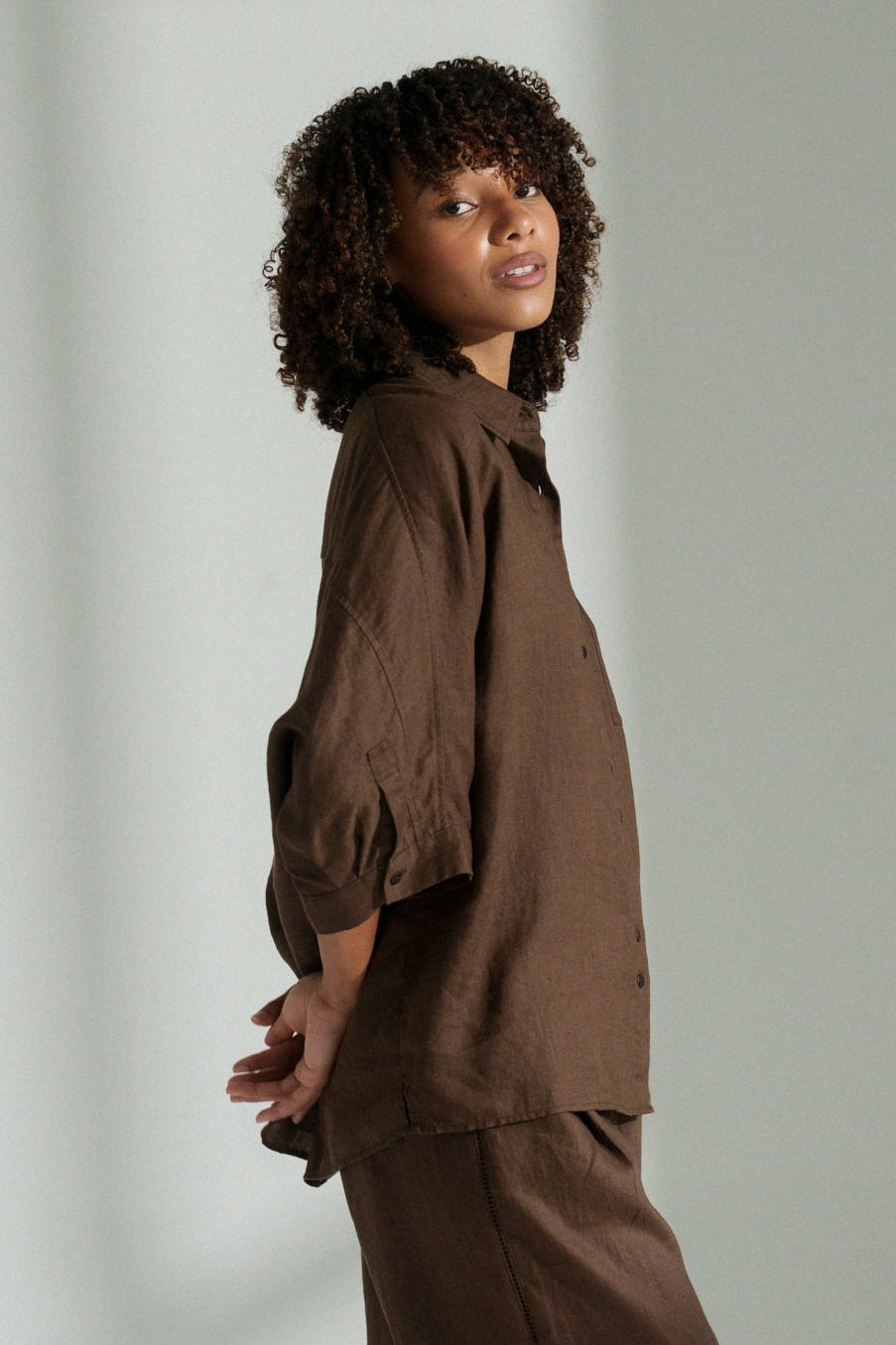 LILLY PILLY woman wearing a chocolate brown Pixie linen shirt and linen pants set showing the side view while against a plain background