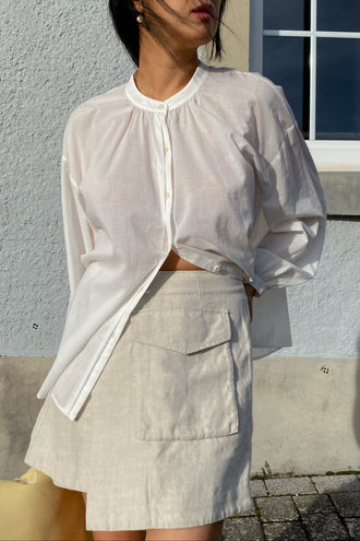Betty Linen Skirt in Oatmeal - front close up view paired with ivory Ember cotton voile shirt standing by a grey wall - Lilly Pilly Collection