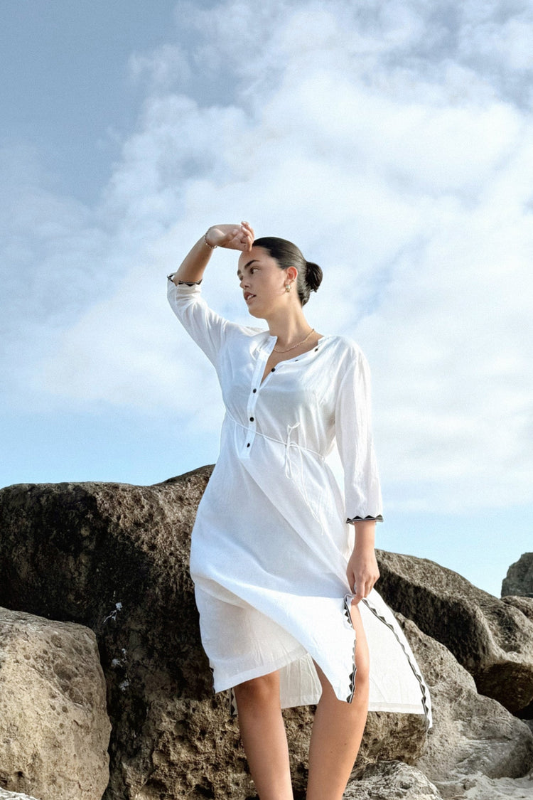 Callie Cotton Voile Midi Dress in Ivory - full length, standing on rocks, tie waist and contrast-trim cuffs, sky backdrop - Lilly Pilly Collection