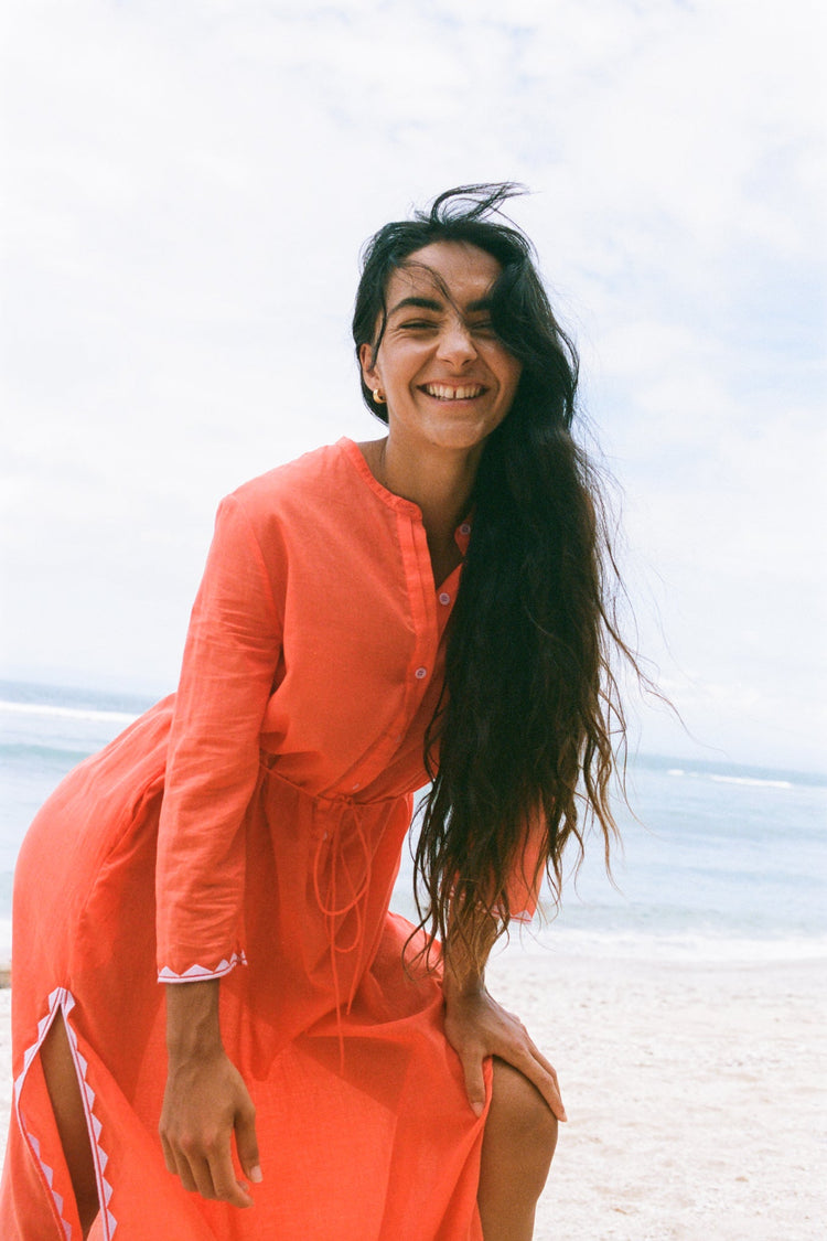 Callie Cotton Voile Midi Dress in Spritz Orange - leaning forward laughing, button placket and tie waist, beach with ocean backdrop - Lilly Pilly Collection