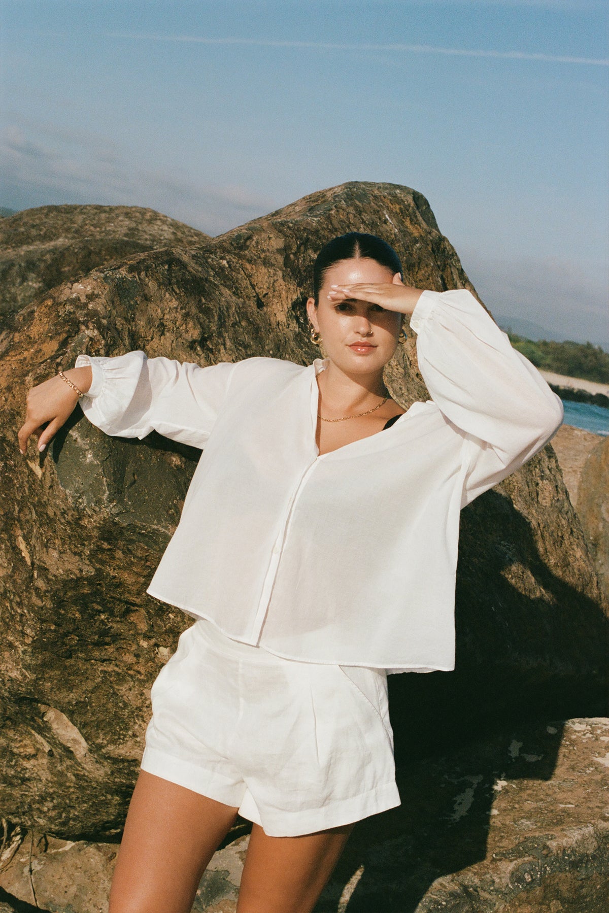 LILLY PILLY woman in an ivory white Ember cotton voile top  standing on a rocky landscape with a scenic background