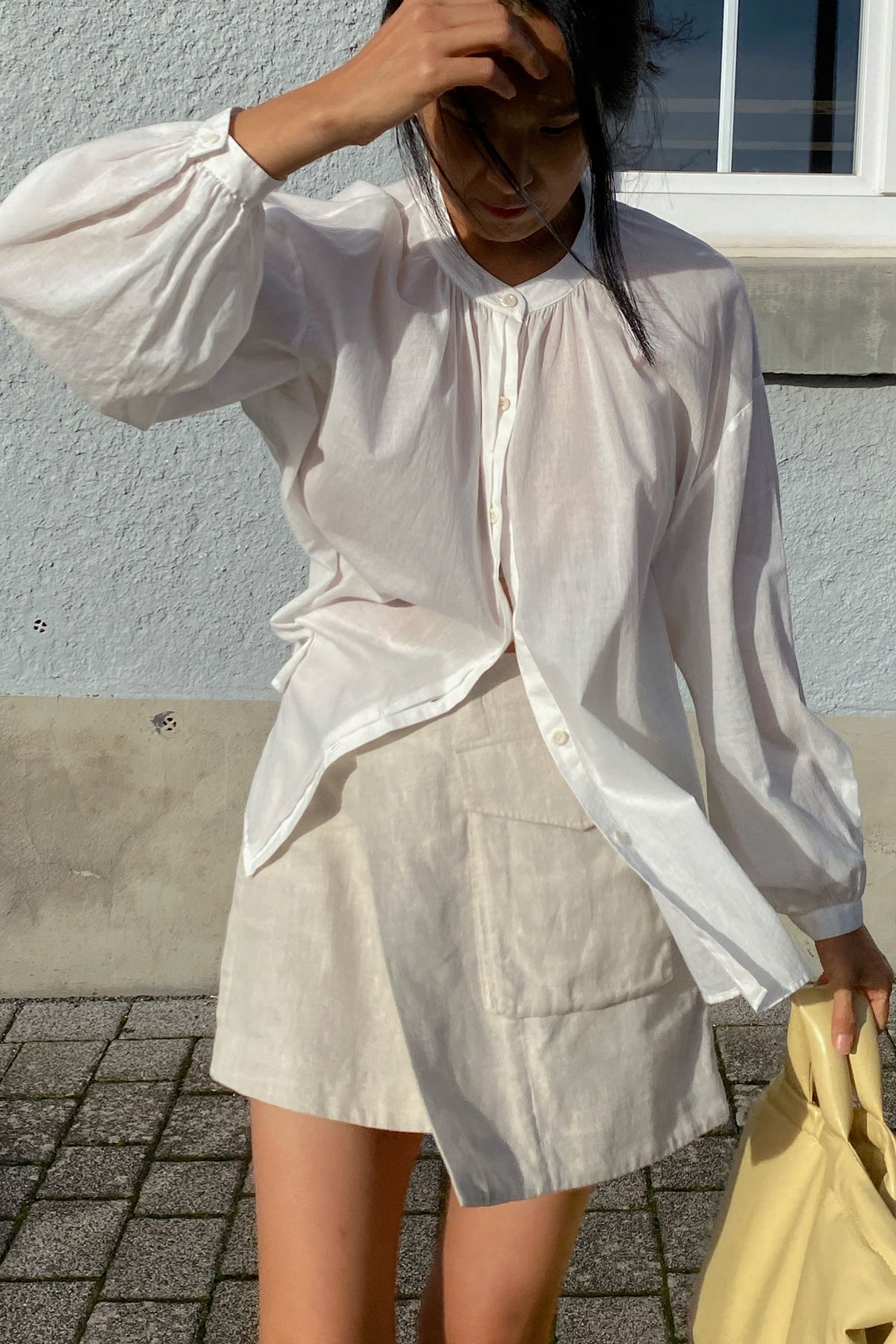 LILLY PILLY woman in an ivory white Ember cotton voile top and beige skirt against a light blue wall.