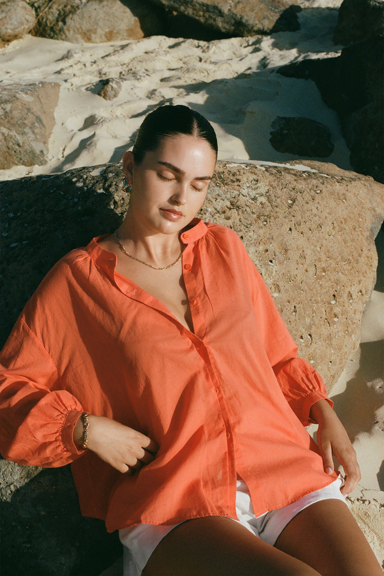 Ember Cotton Voile Shirt in Spritz Orange - front view while seated against the rocks - Lilly Pilly Collection