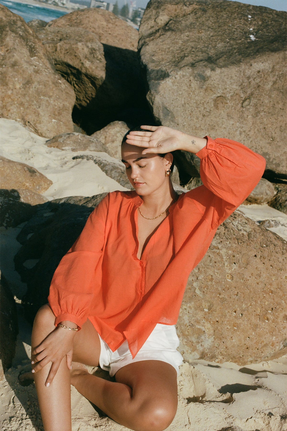 LILLY PILLY woman in a spritz Ember cotton voile top sitting on a rock by the sea.