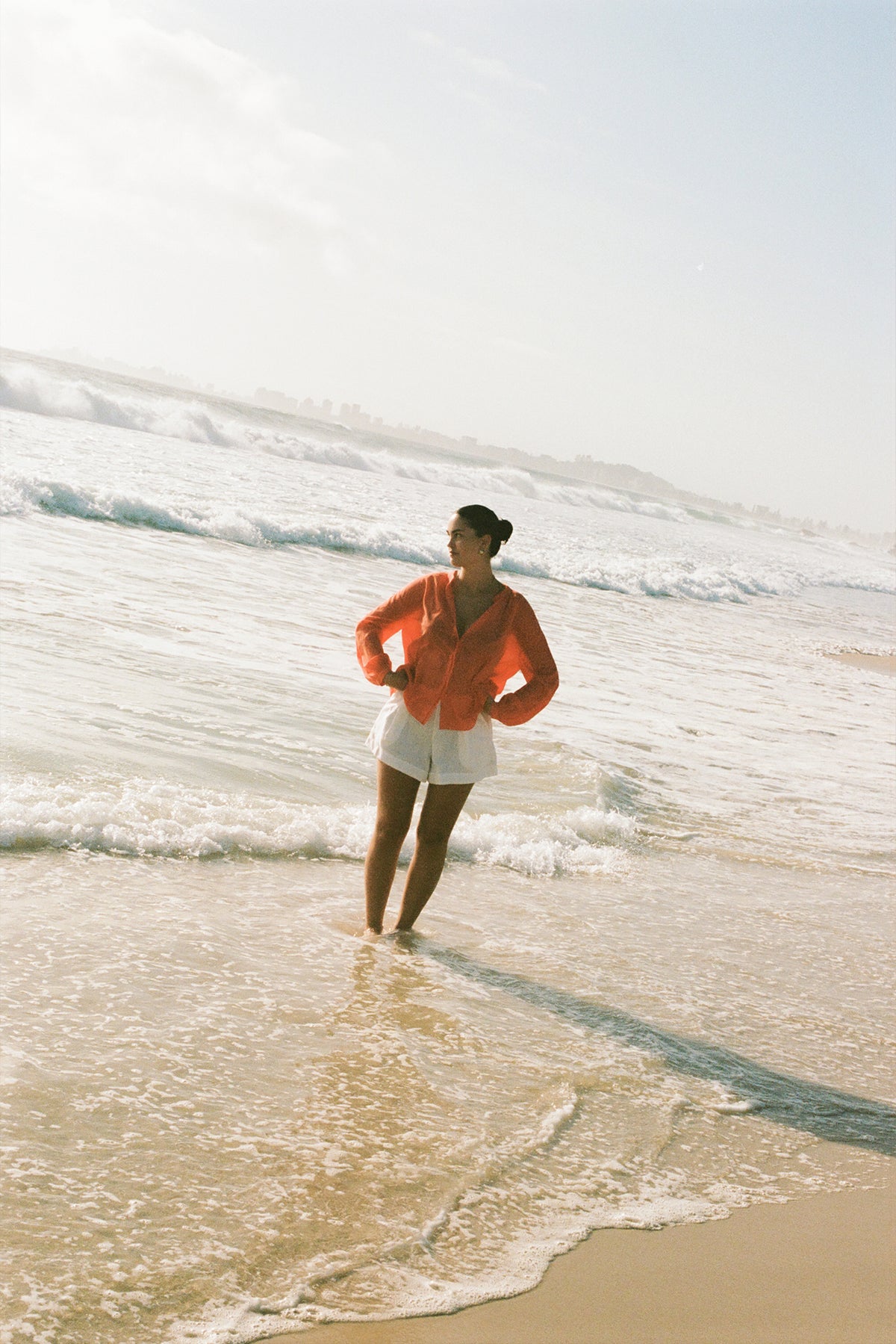 LILLY PILLY woman in a spritz Ember cotton voile top and white shorts standing in shallow water at the beach