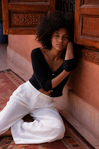 Jade Cashmere Cardigan in Black - sitting, V-neckline and button-front, worn with wide-leg trousers, resting head on arm, Moroccan doorway backdrop - Lilly Pilly Collection