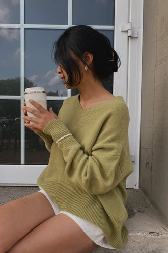June Cashmere Knit in Olive - sitting, holding coffee cup, worn with Gaia Linen Shorts in Ivory, outdoor setting - Lilly Pilly Collection