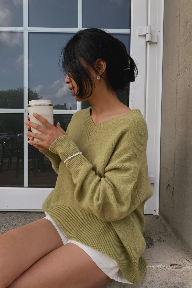 June Cashmere Knit in Olive - sitting, holding coffee cup, worn with shorts, outdoor setting - Lilly Pilly Collection
