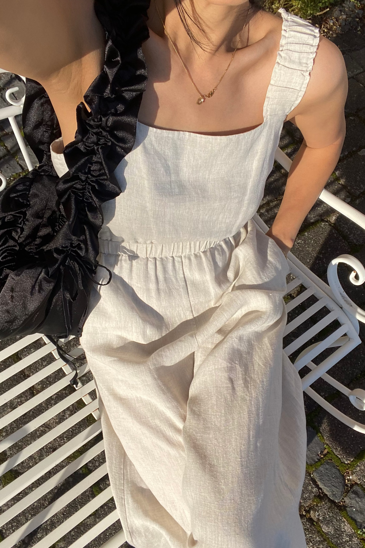 Close-up of a woman wearing the Keely Linen jumpsuit in Oatmeal with a black shoulder bag- Lilly Pilly Collection