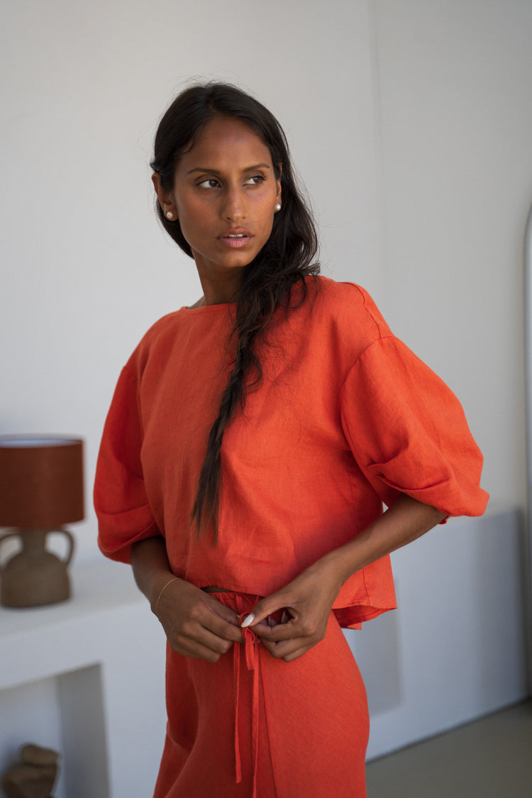 Leia Linen Top in Spritz Orange - front view, tying waist tie, round neckline and puff sleeves, worn with matching pants, studio setting - Lilly Pilly Collection