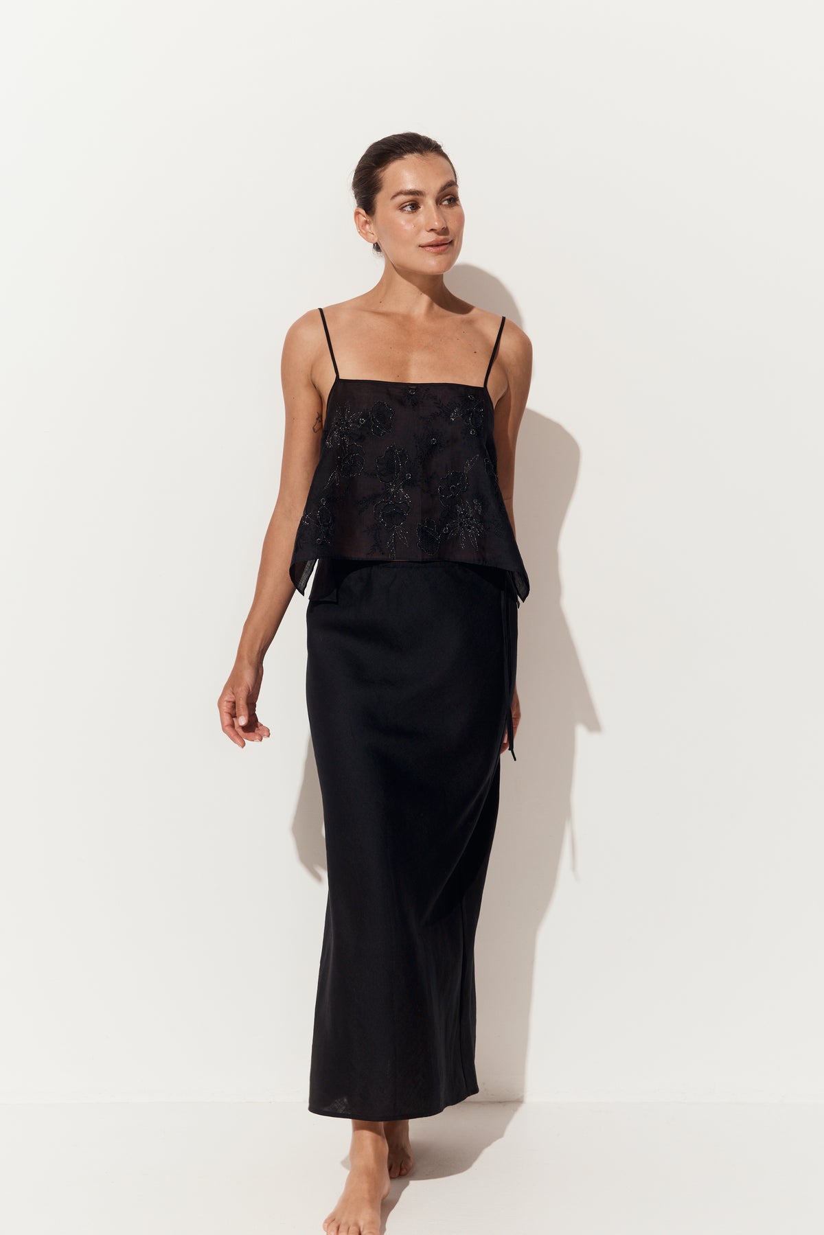 Riley Bias Linen Skirt in Black - front view walking, styled with a beaded cami, white studio backdrop - Lilly Pilly Collection