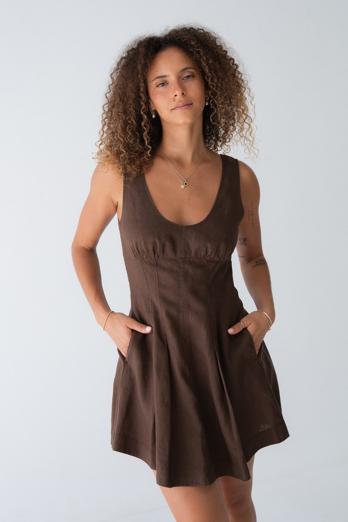 Adele Linen Short Dress in Chocolate - full front view, hands in pockets, scoop neckline and pleated skirt - Lilly Pilly Collection