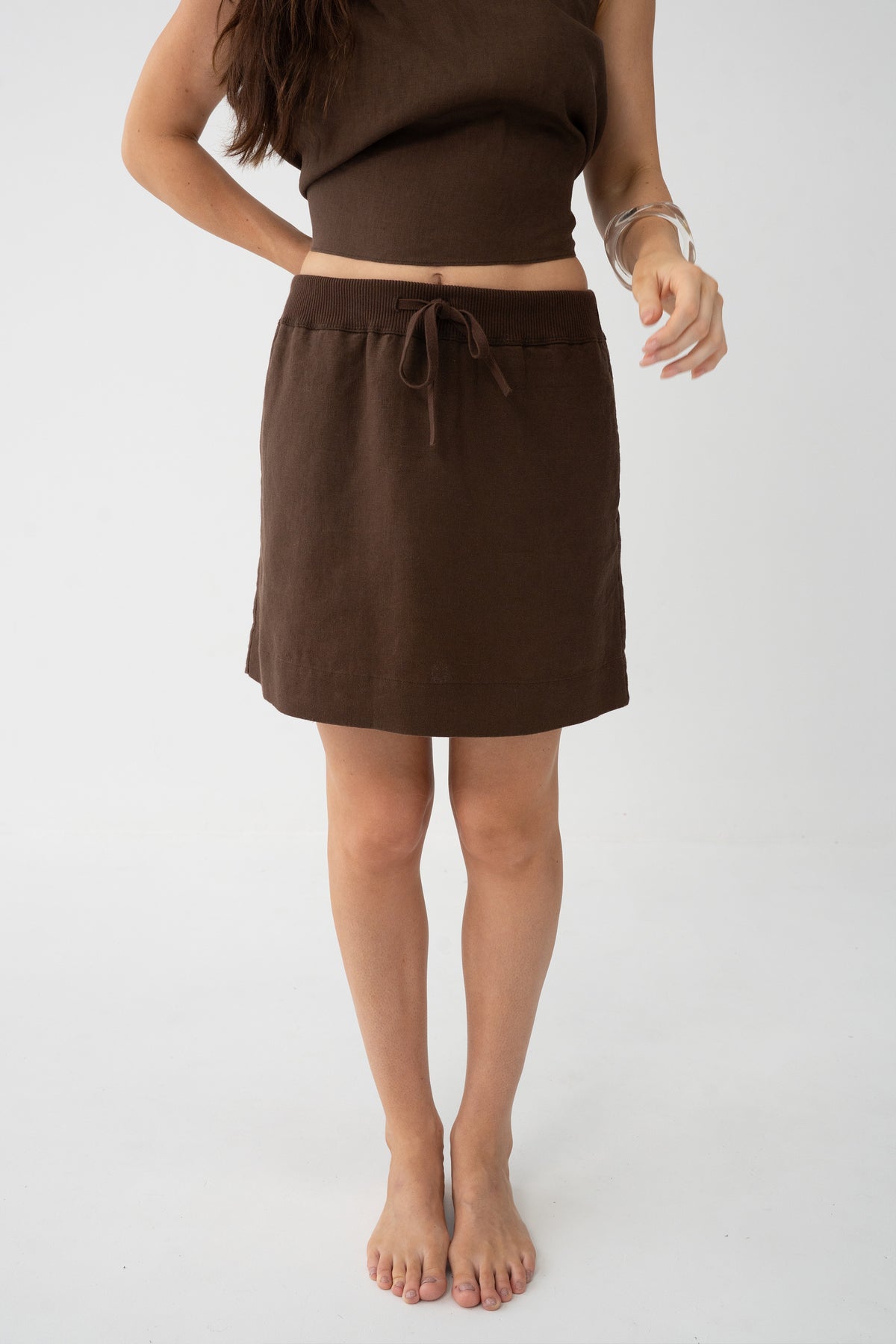 Anelle Linen Mini Skirt in Chocolate - front view, drawstring waistband and elasticated waist, silver bracelet - Lilly Pilly Collection
