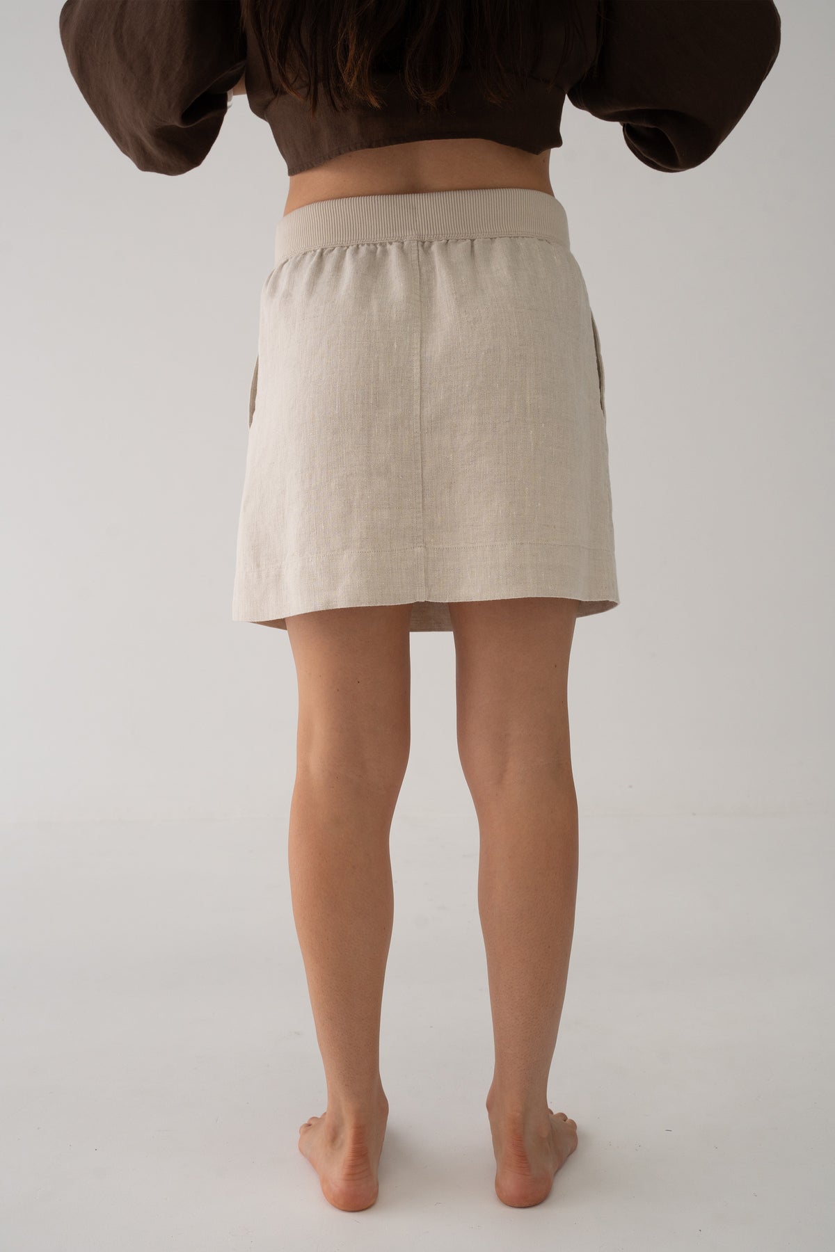 Anelle Linen Mini Skirt in Oatmeal - back view, elasticated waistband, worn with Tilly Cotton Voile Shirt in Chocolate - Lilly Pilly Collection