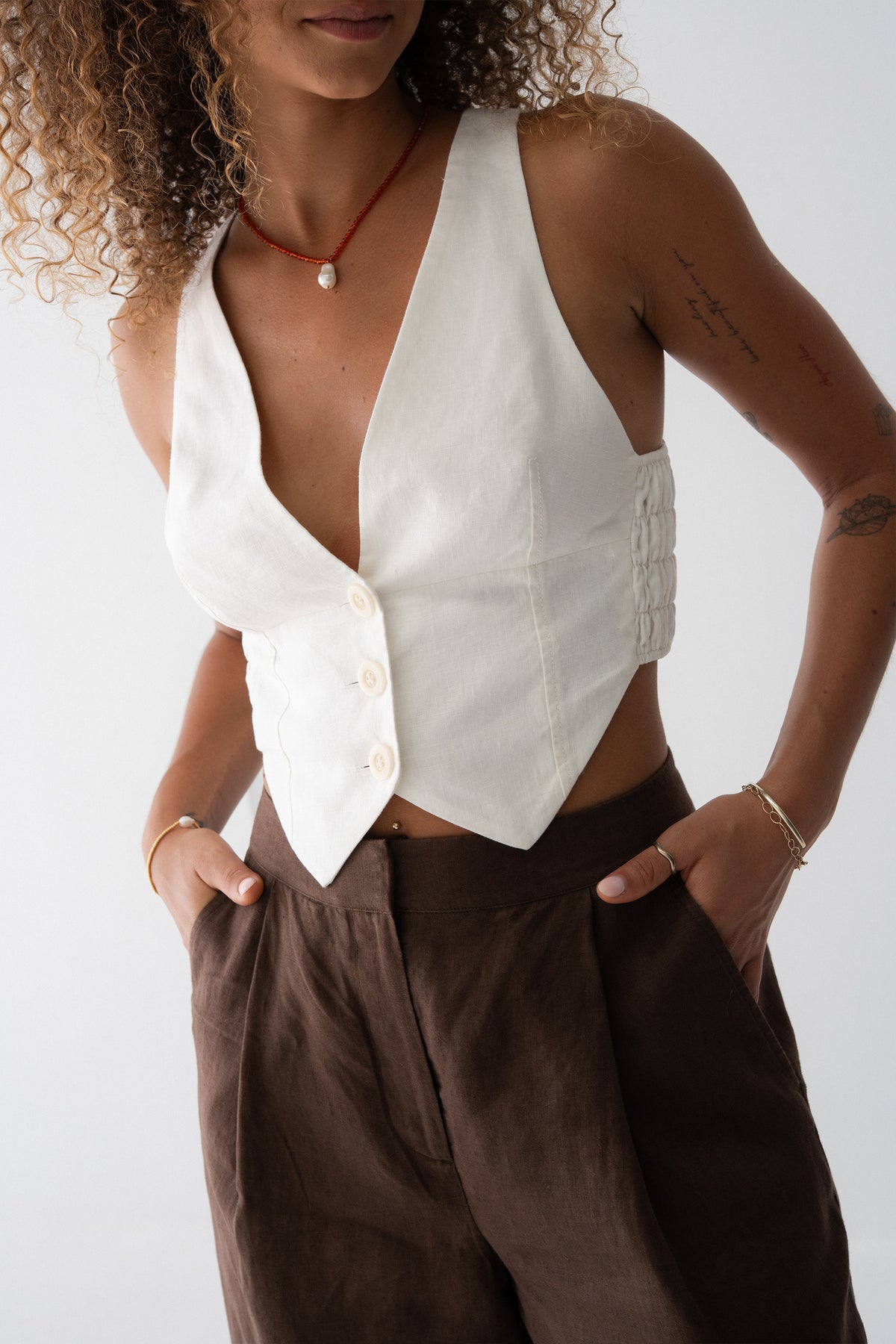 Ari Linen Vest in Ivory - close-up of deep V-neckline, button-front and pointed hem, styled with chocolate wide-leg linen pants - Lilly Pilly Collection