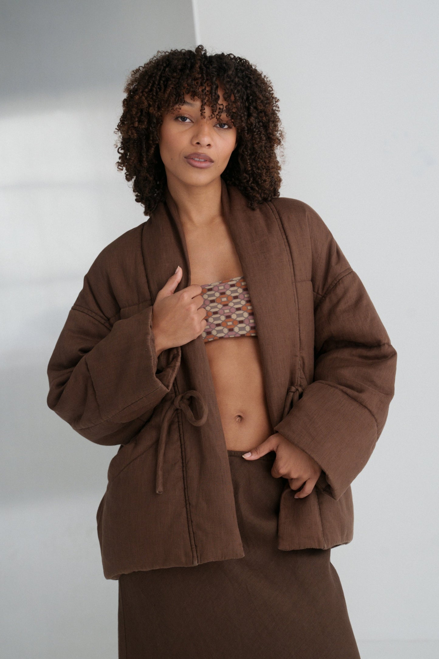 LILLY PILLY woman wearing a chocolate brown Aster linen jacket over a patterned top against a white background