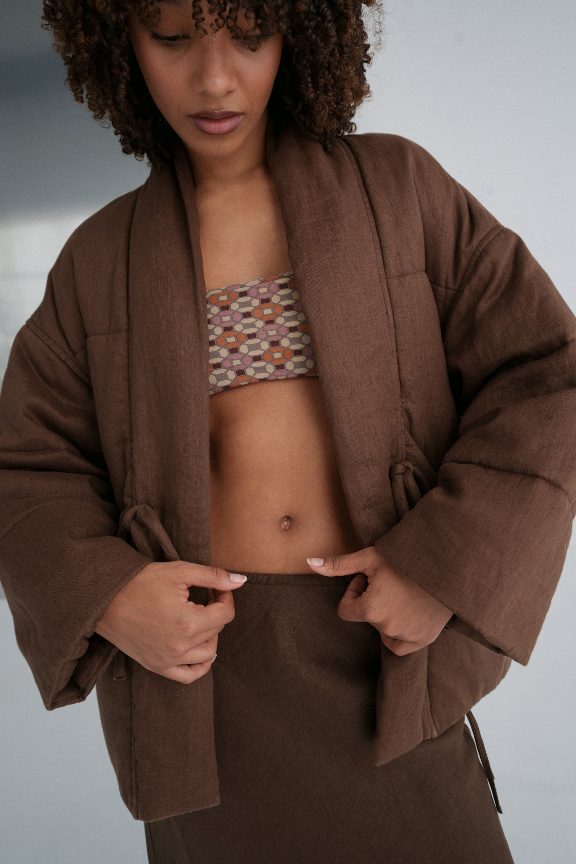 LILLY PILLY woman wearing a chocolate brown Aster linen jacket over a patterned top against a neutral background