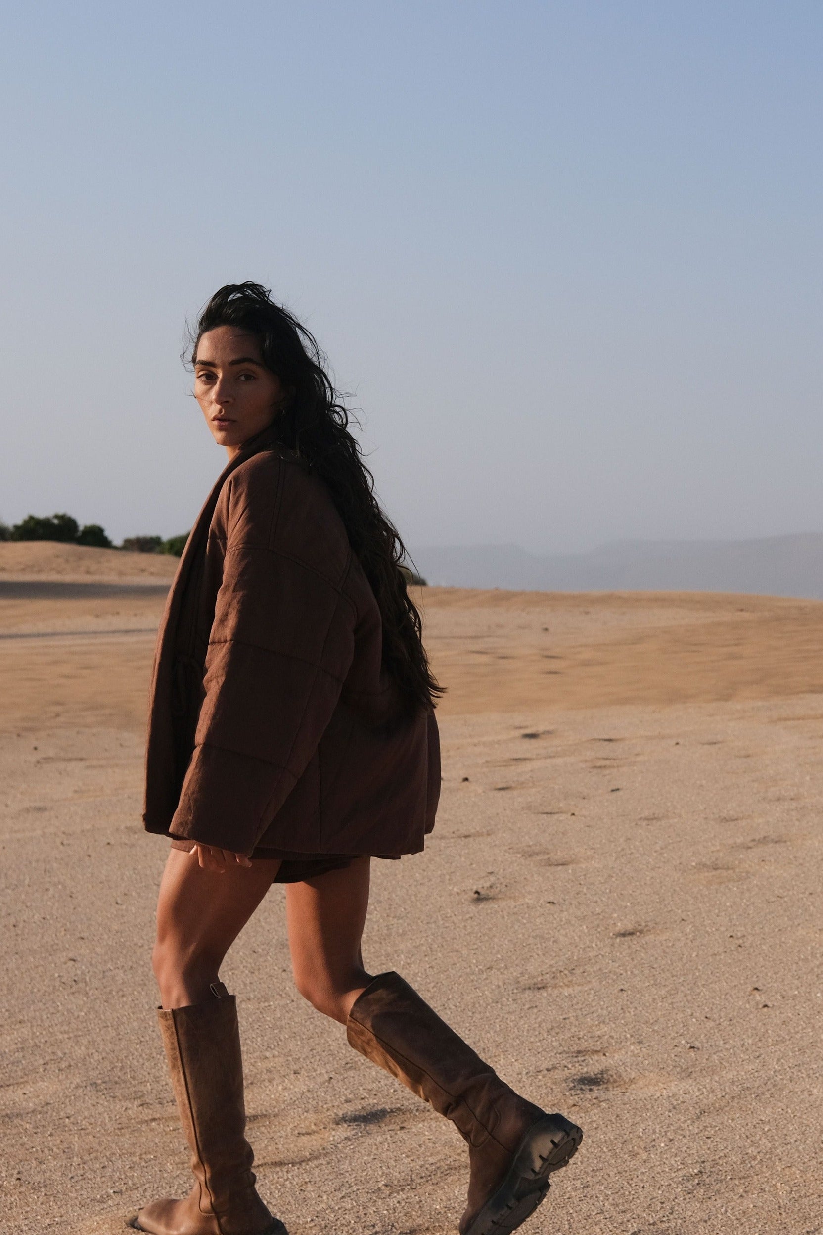 LILLY PILLY woman wearing a chocolate brown Aster linen jacket walking in a desert landscape with clear sky