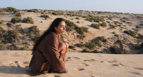 LILLY PILLY woman wearing Aster linen puffer jacket in chocolate while sitting in the sand dunes