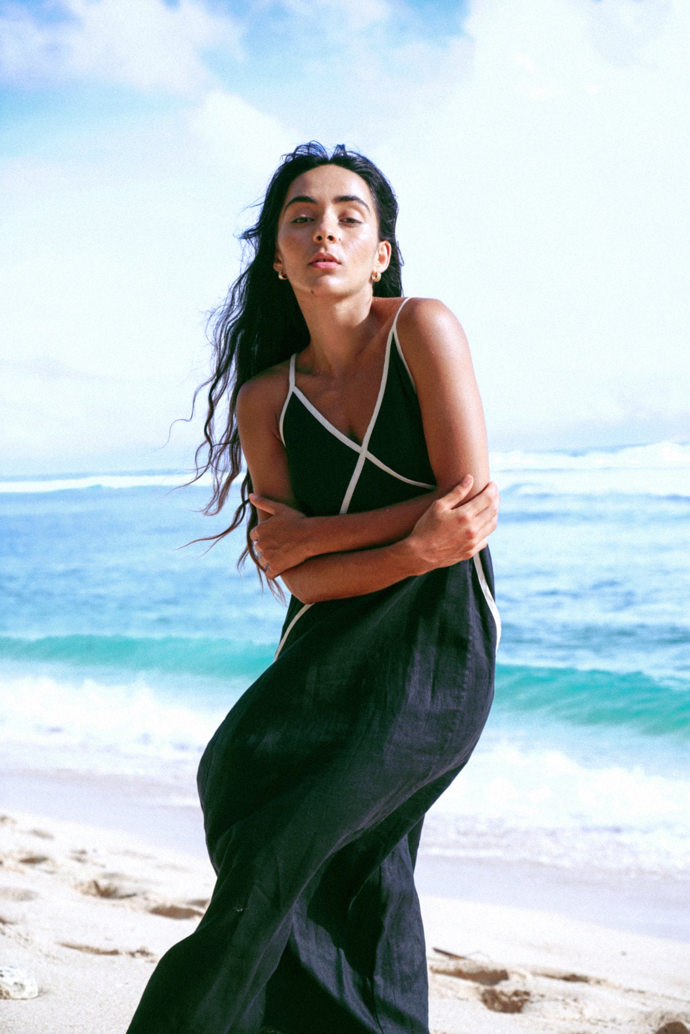 LILLY PILLY woman in a Azalea black linen dress standing on a beach with ocean and sky in the background