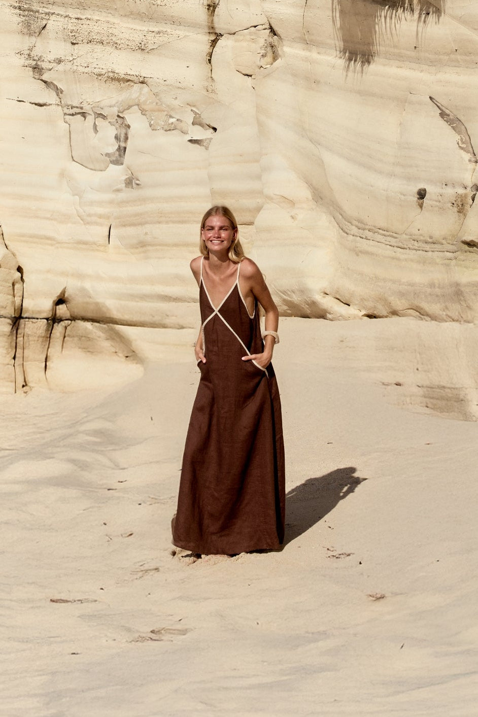 Azalea Linen Maxi Dress in Chocolate - full length view, fluid maxi silhouette and contrast trim, beach cliffs backdrop - Lilly Pilly Collection