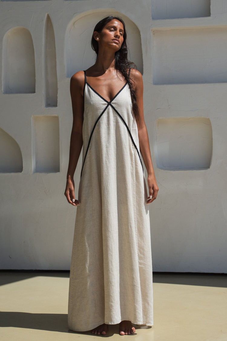 Azalea Linen Maxi Dress in Oatmeal - full front view, V-neckline with contrast black trim, architectural backdrop - Lilly Pilly Collection