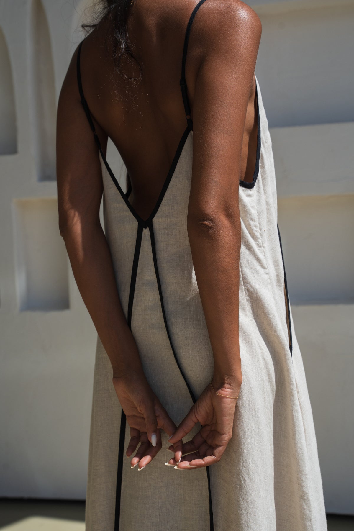 Close up back view of Lilly Pilly woman wearing an oatmeal Azalea dress with black straps in an abstract indoor setting